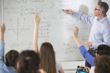 Male teacher leading physics lesson at whiteboard in classroom