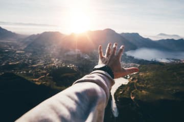 arm reaching towards mountains