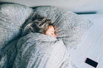 Woman sleeping in bed with her phone beside her