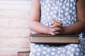 persons hands folded on bible