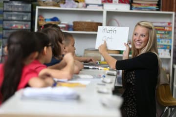 teacher holding whiteboard and teaching students