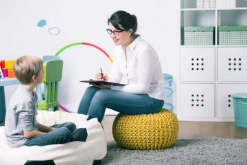 A family therapist sits in playroom and asks a little boy questions