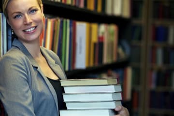 Attractive blonde woman holds stack of books in library