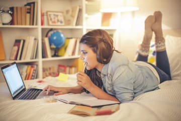 student doing homework on her bed