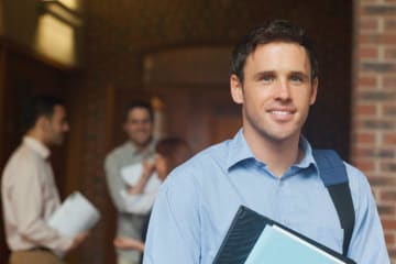 Adult male student holds folder and wears backpack on one shoulder with two males in background