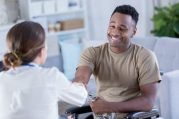 Female doctor shakes hand of African-American male patient who is smiling in wheel chair