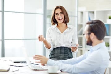 Woman laughs in an open office space while a man sits at a desk