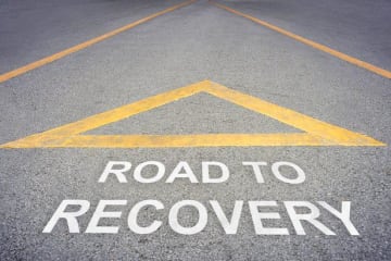 Yellow upright triangle above road to recovery lettering on a road