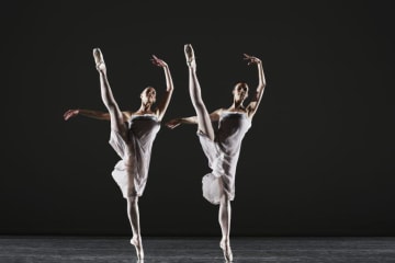 Two ballerinas dancing on stage, legs raised