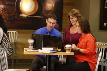 Group of adults gather around a laptop to look at it