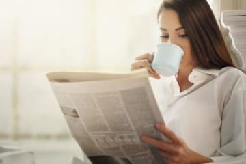 girl reading newspaper and sipping out of a mug