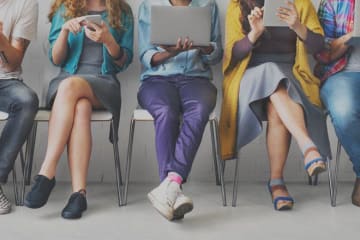 Front view of millennials sit in a row using phones and tablets