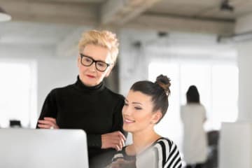 A woman at a computer with an older woman helping her