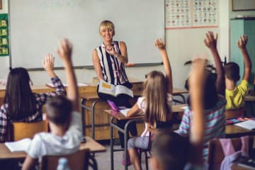 Teacher points out student in classroom of raised hands