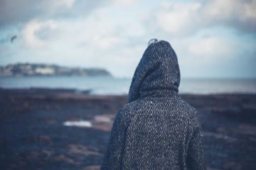 Back of hooded individual looking out at a barren landscape