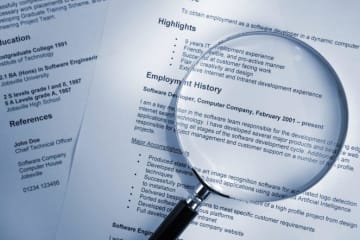 A stack of resumes with a magnifying glass on top