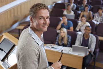 Male instructor stands next to podium with a full auditorium of students