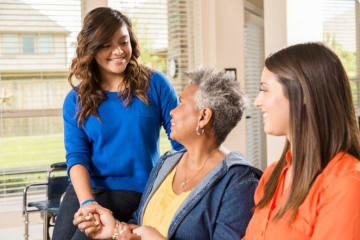 Young woman smiles holding hand of older woman with a third woman seated next to her