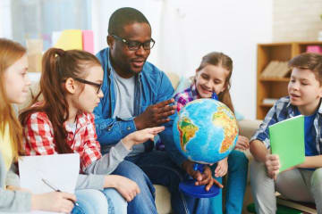 teacher holding globe and surrounded by young students