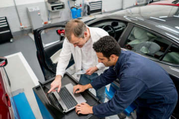 Man working on a computer by a car