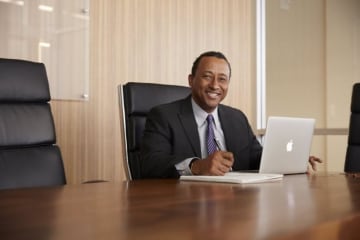 Smiling man in suit and tie sits in conference room with laptop open