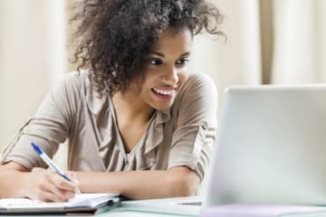 girl looking at computer and writing in a notebook