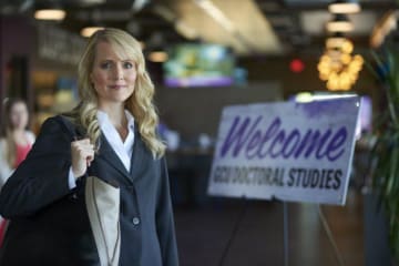 Blonde woman in professional clothing stands at entrance for doctoral studies mixer