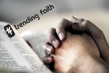 Hands clasped in prayer position on top of open bible with hashtag trending faith text on top