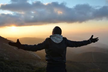 A man spreading his arms at the top of a mountain at sunset