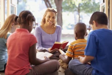 Teacher reads aloud to students sitting on the ground