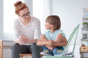 Female behavioral health counselor sits with young boy in play room