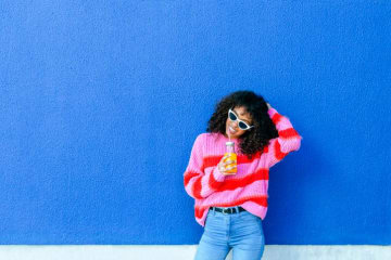 a girl sitting against a wall and drinking orange juice