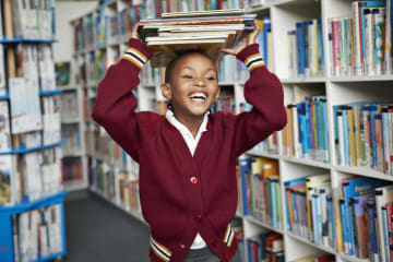 Girl stacks thin books atop her head in library