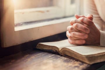 man with folded hands praying on a bible