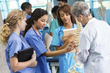 three nursing students and professor looking at a skeleton