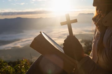 Woman praying over Gods word with a cross