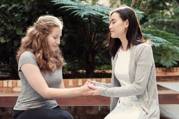 Two girl friends praying on a bench together showing humility before God