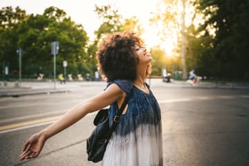 Curly-haired woman has arms open enjoying the sunlight in an empty parking lot