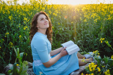 Woman looking up after reading her Bible in a field of flowers for spiritual cleansing