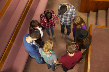 Christians standing and holding hands while praying for one another near church pews