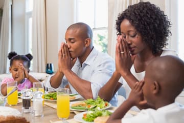 Family praying at the dinner table bearing with one another in love