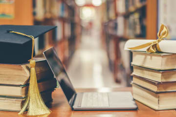 A stack of books next to a graduation cap and a laptop