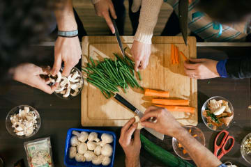 diverse hands prepare food around a cutting board in kitchen setting