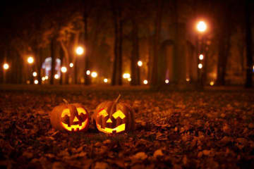 Jack-O-Lanterns lit on a dark road with fall leaves