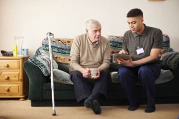 young male social worker meeting with elderly male client on couch