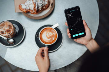 Person investing on their phone in coffee shop