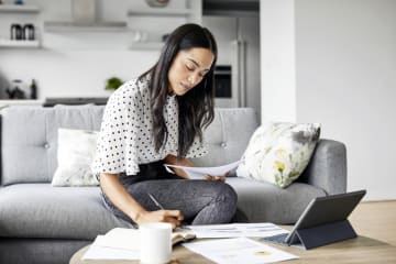 Woman sitting on gray couch in professional wear working on finances at home
