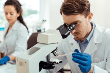 Biologist studies sample through a microscope in a lab