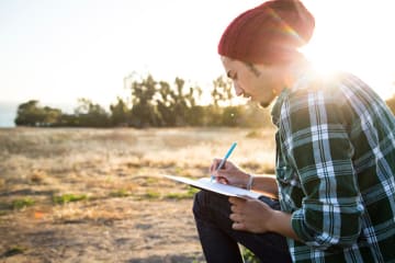 A male college student practicing daily journaling by writing outside alone