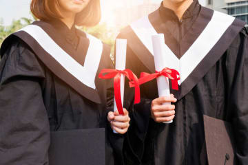 Two college graduates holding their diplomas and wearing their cap and gown